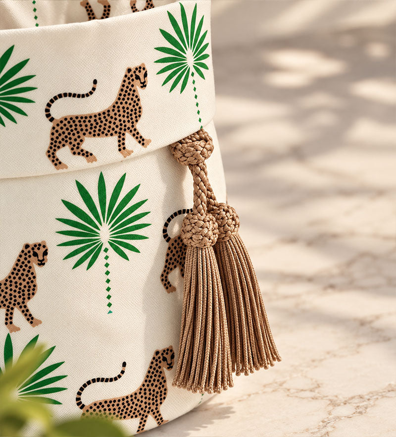 Dettaglio delle nappine beige intrecciate e della stampa con felini e palme verdi sul cestino Gattopardo.